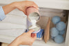 A woman measuring oxi laundry booster into the forever tin lid next to a linen closet