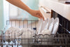 A person loading clean dishes into a dishwasher, organizing them for efficient cleaning and space management.