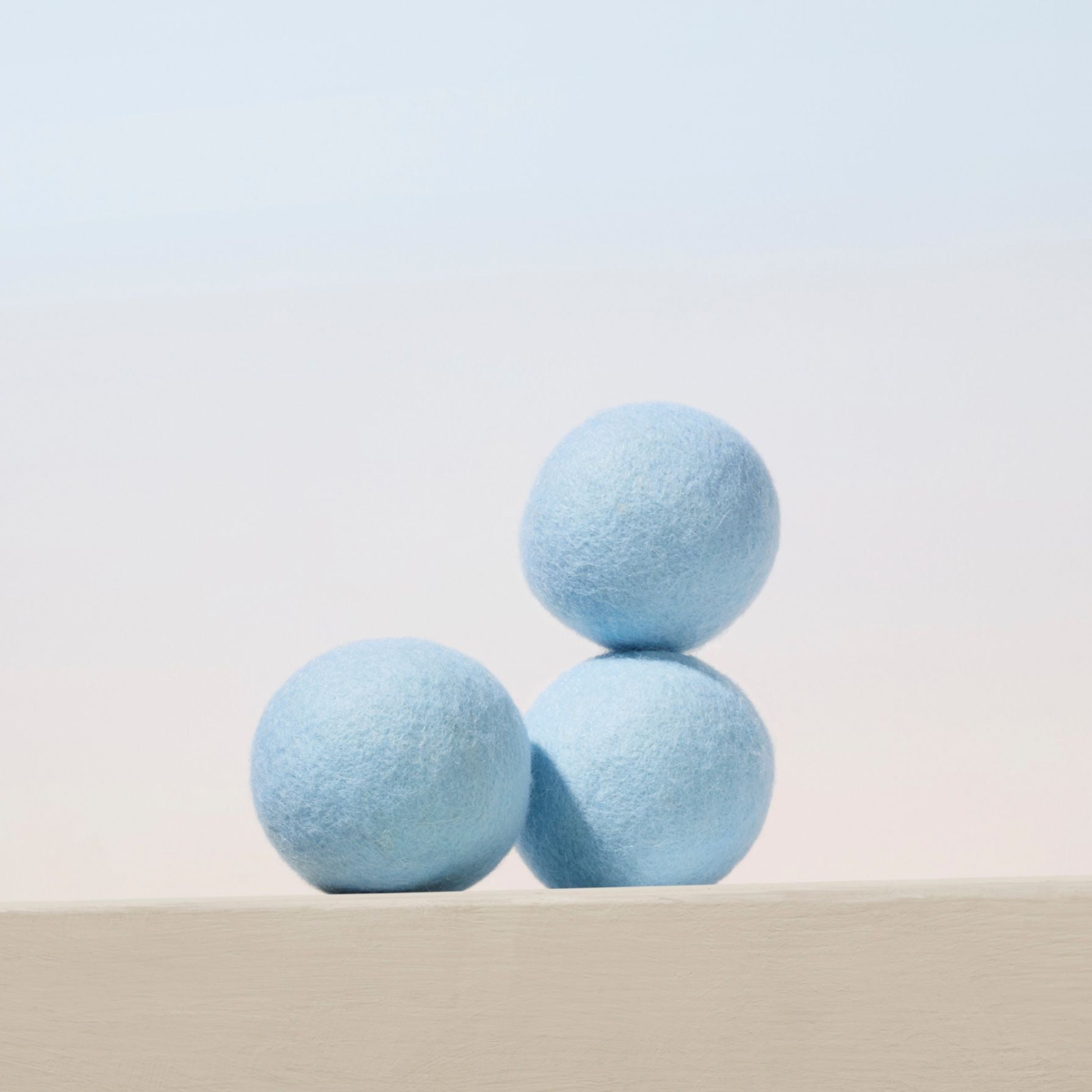 Three light blue dryer balls stacked on a light gray surface with a light gray background