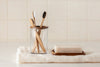 Bamboo toothbrushes in a glass holder next to a bar of soap on a towel in a minimalist bathroom setting