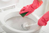 Bright pink gloves cleaning a toilet with a sponge and brush
