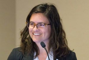 Woman speaking into a microphone at an event with a neutral background