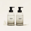 Two clear glass pump bottles labeled BLUELAND Hand Soap are filled with liquid. Next to the bottles are three white tablet-shaped soap refills stacked on a cream-colored surface with a plain background.