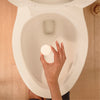 A toilet cleaner tablet being dropped into a toilet bowl